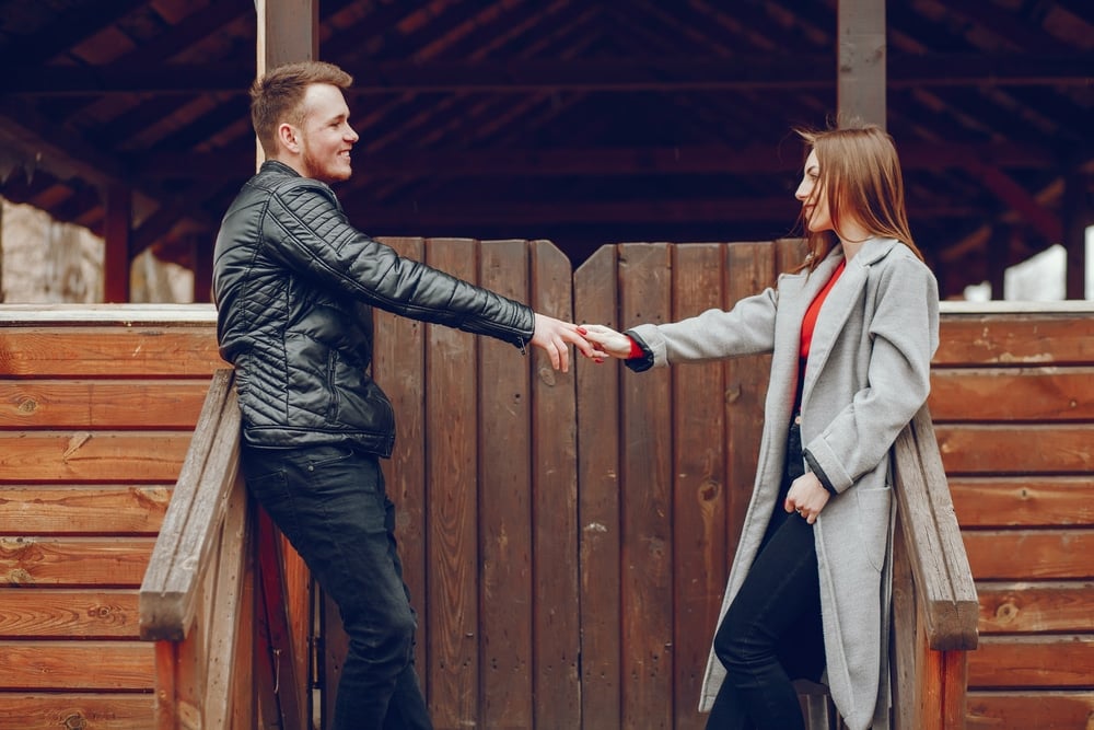 A man and woman outside, holding hands, looking at each other, and smiling.