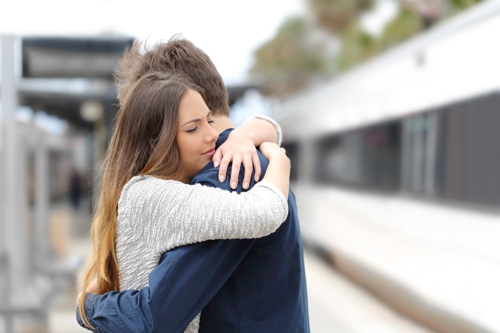 A sad couple embraces, saying goodbye before one leaves for the train.