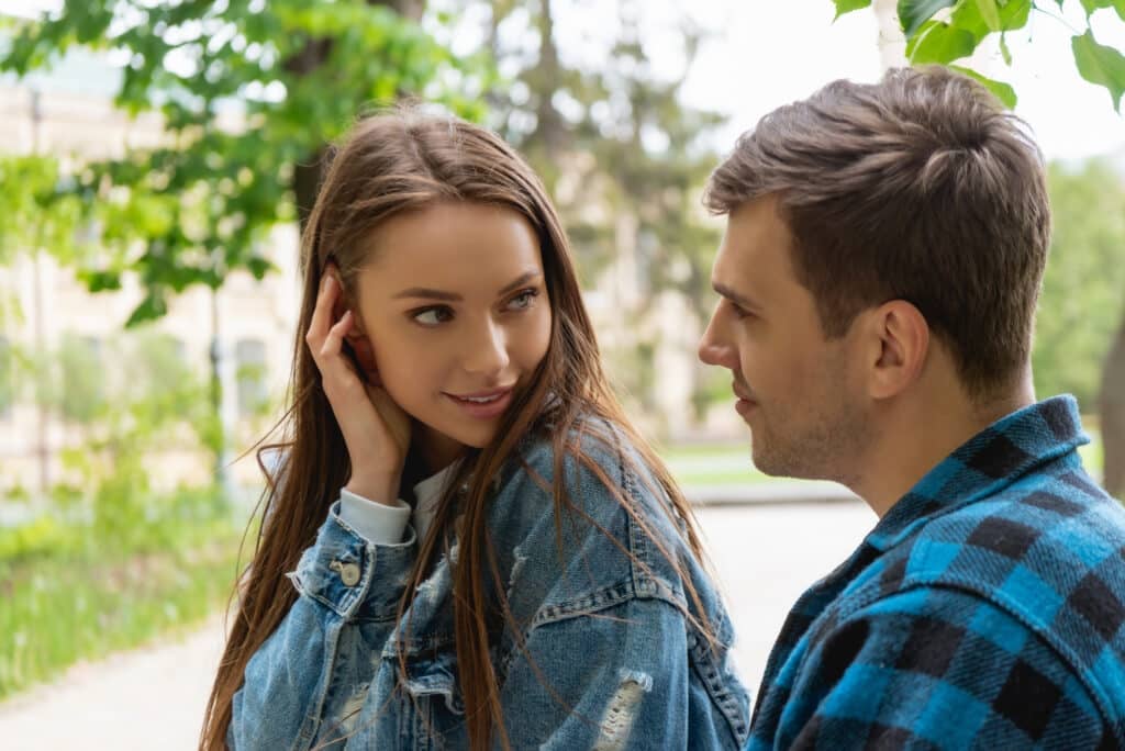 An attractive young lady looks over her shoulder as she brushes her hair while glancing at a guy she likes outside.