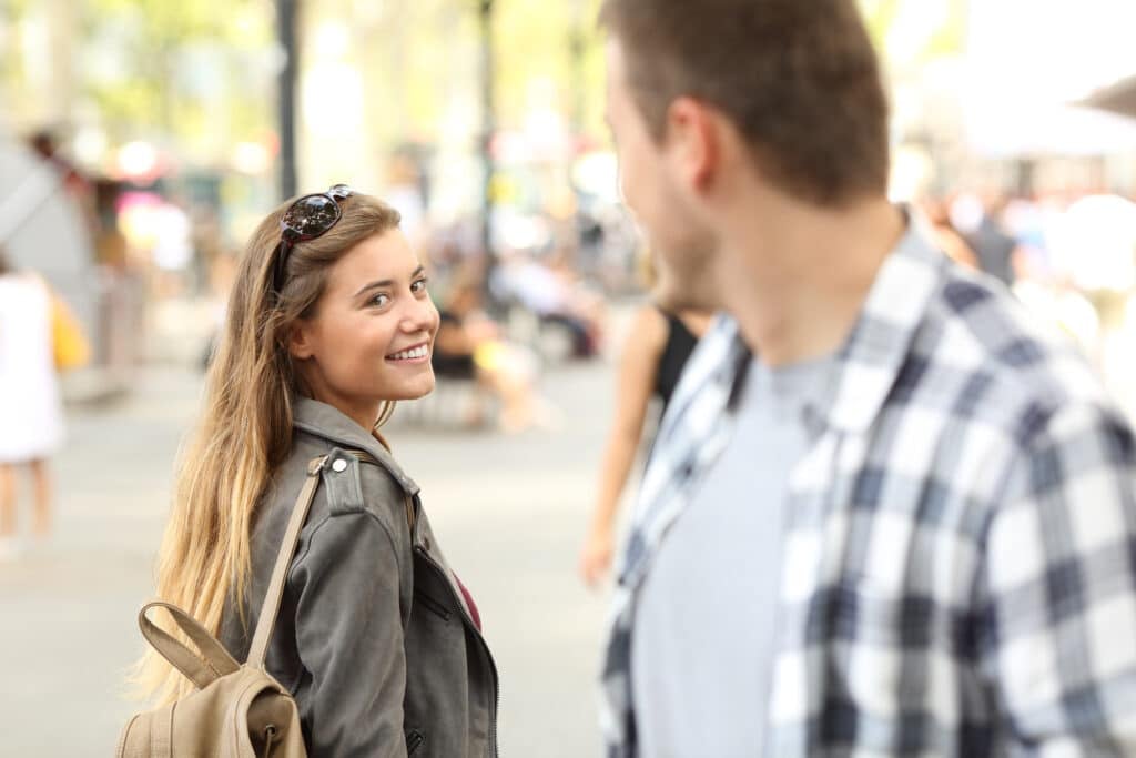 Strangers meet on the street, where a girl and a guy flirt and exchange smiles.