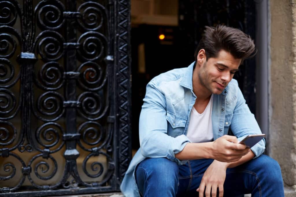 Handsome young man sending a text message while sitting outside on steps.