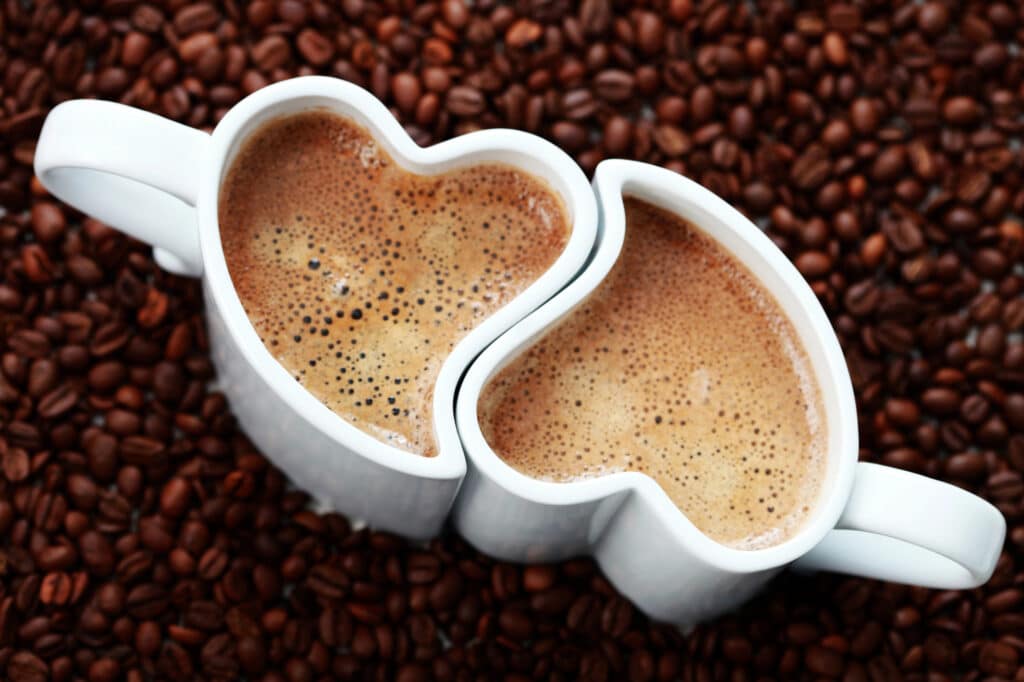 Two heart-shaped mugs connected by coffee beans, signifying love.