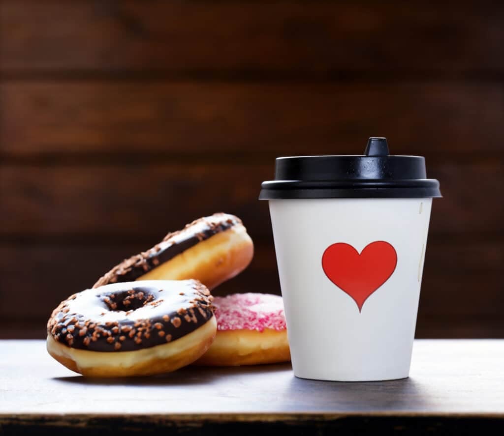 Coffee cup with a red heart and sprinkled donuts beside it on a table.