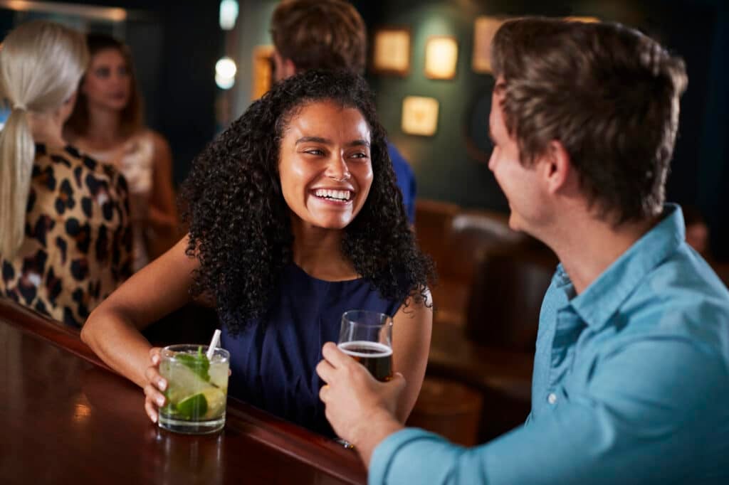 A couple on a date chats and laughs while sitting at the bar counter, enjoying drinks and conversation.
