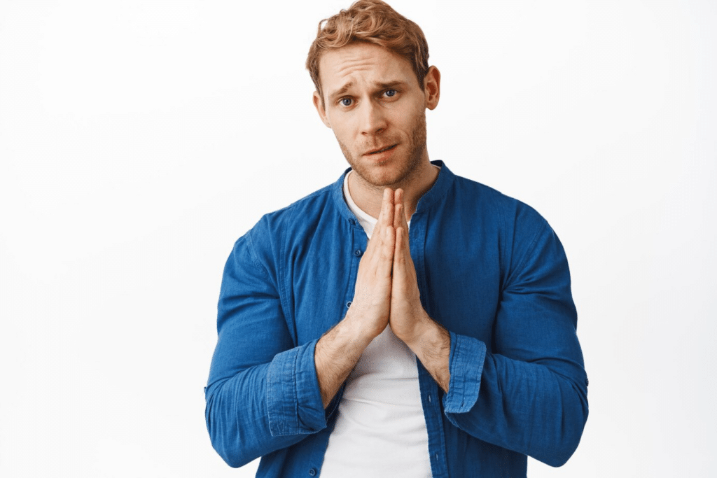 A man in a jean shirt claps his hands together as he asks for forgiveness.