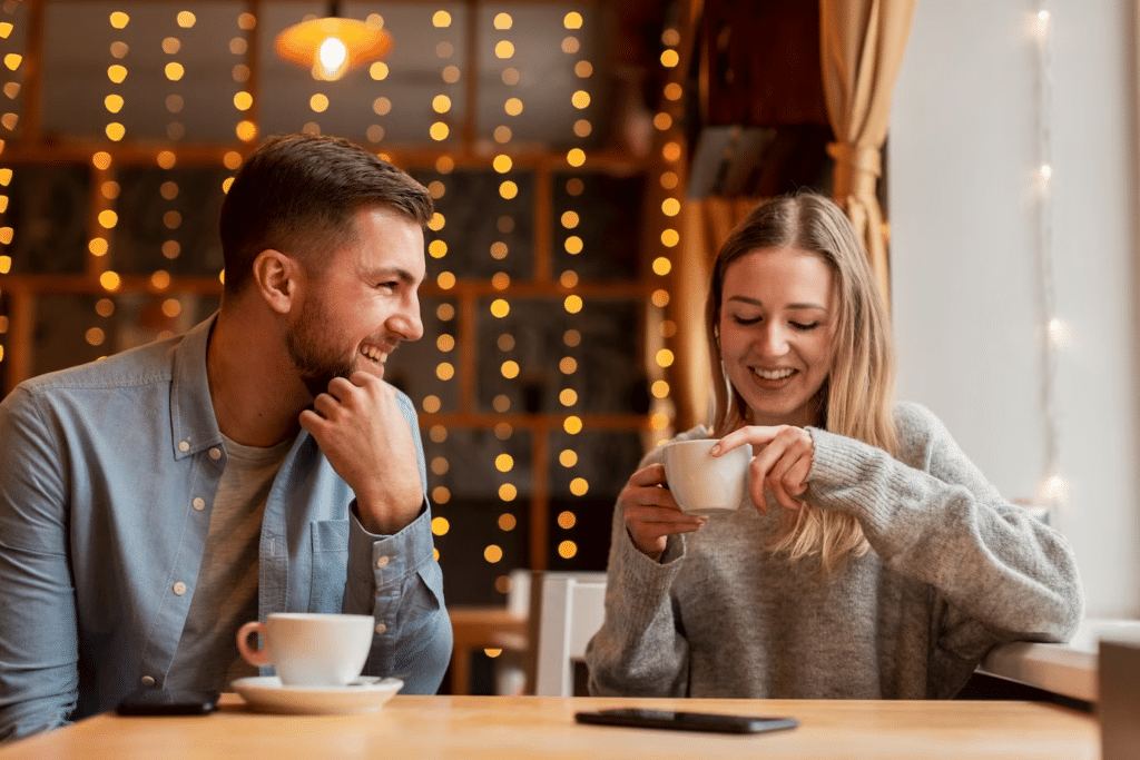 A young couple is laughing and chatting at a cafe, while the young lady holds a cup with streamers in the background.