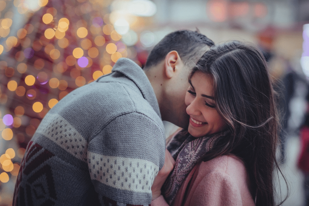 Man kissing a woman on her cheek as they stand close together outside.