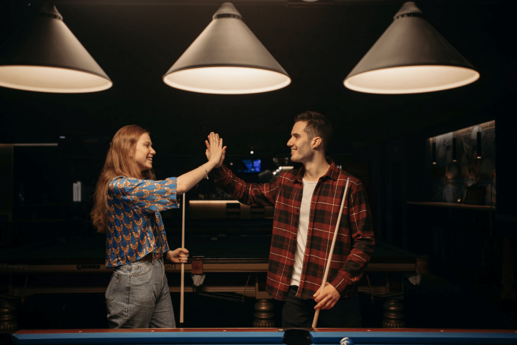 Man and woman high fiving each other while playing billiards in a bar.