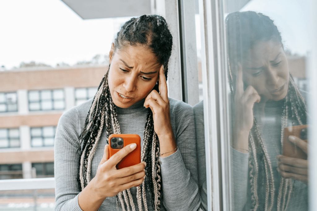 Woman standing on a balcony looking at her phone sadly after being rejected.