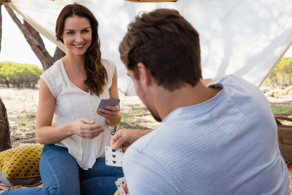 A lady smiles with a guy outside as they play cards under a tent.